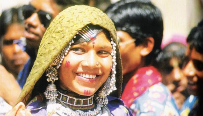 Tribal women in colorful traditional outfits performing rituals by the river at the Chitra Vichitra Mela in Gujarat, surrounded by greenery and festive decorations.