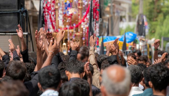 People participating in a Muharram procession with traditional banners and symbols