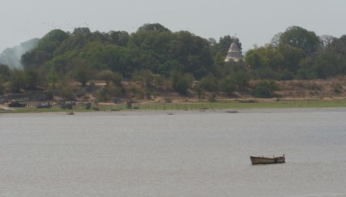 A serene riverside view at Kabirvad Camping Site, surrounded by large banyan trees and peaceful natural settings